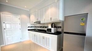 Una cocina moderna con armarios blancos, un refrigerador de acero inoxidable, un microondas y una tetera sobre la encimera.