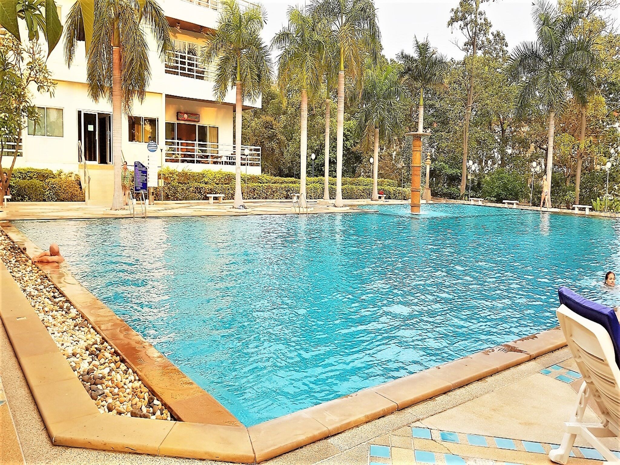 A swimming pool with a tiled edge, surrounded by palm trees and a building with a sign that reads "Spa House".