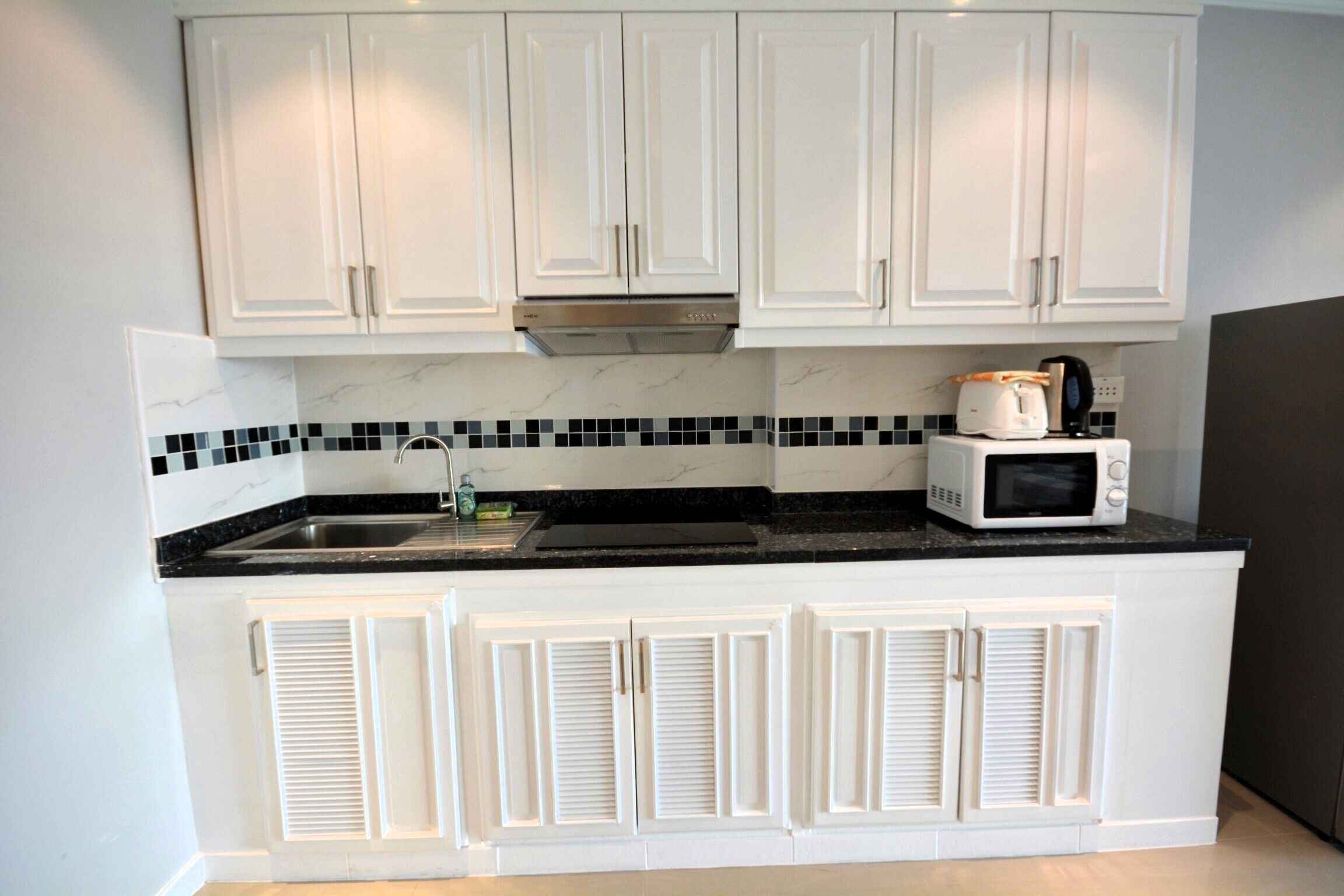 A kitchen with white cabinets, a black countertop, and a microwave.
