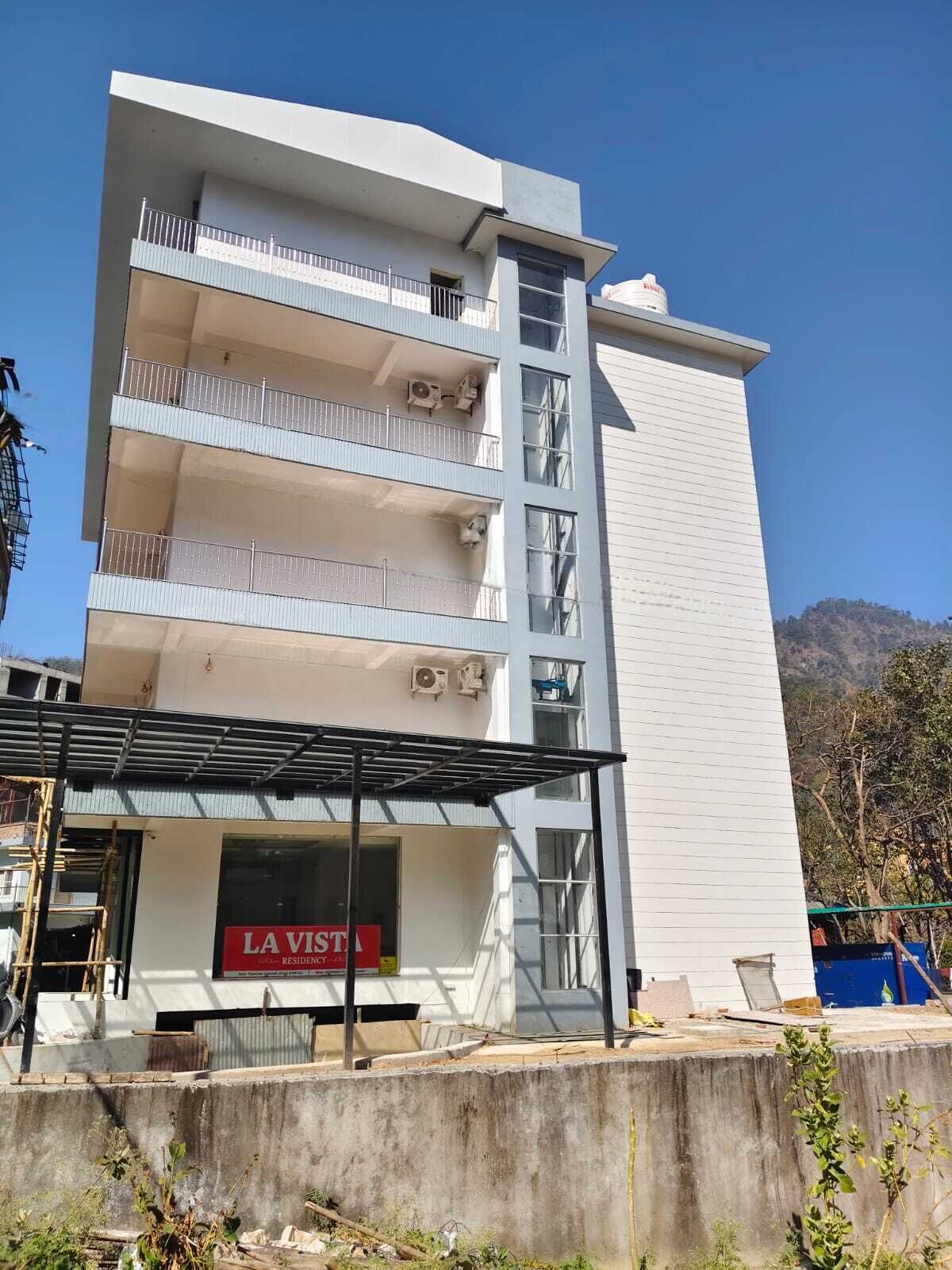 Un edificio de varios pisos con balcones, un letrero que dice "LA VISTA RESIDENCY" y un cielo despejado al fondo.