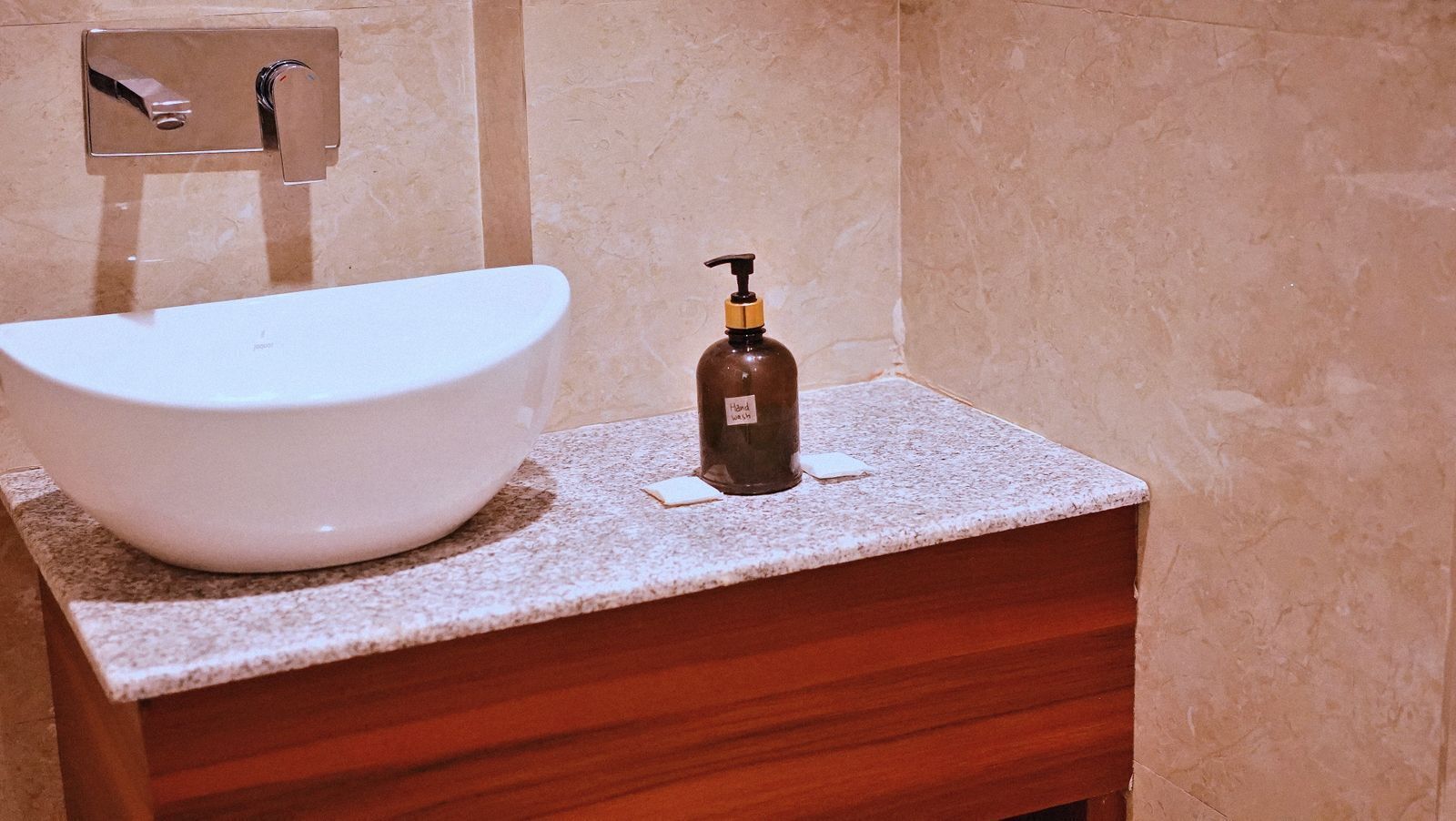 A bathroom with a white vessel sink, a soap dispenser, and a marble countertop.