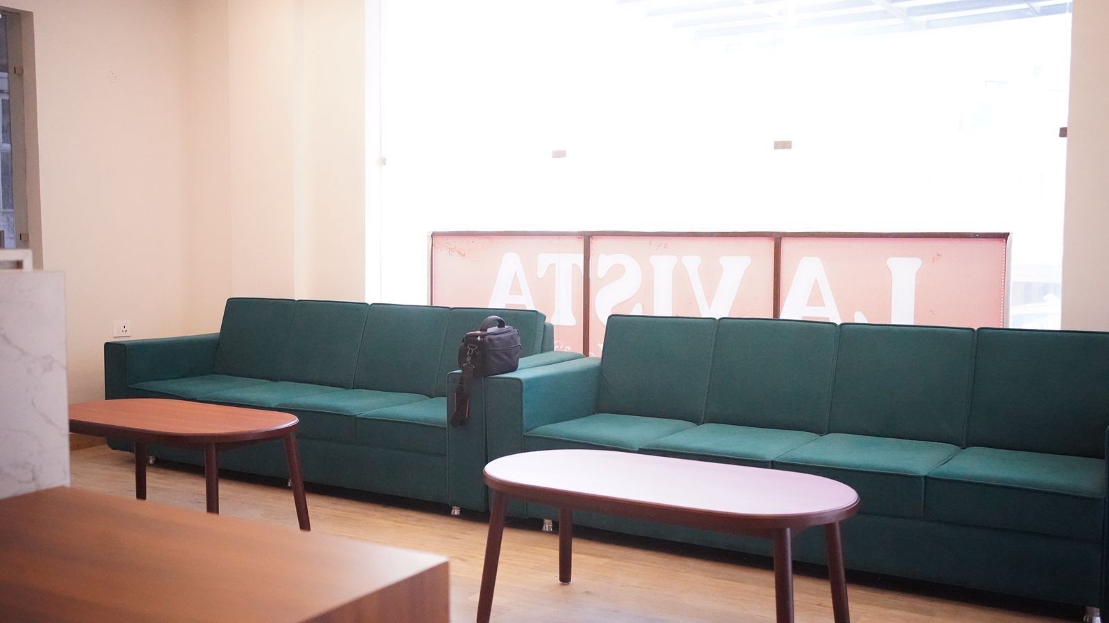 A room with a green sofa, two wooden tables, and a large window with a view.