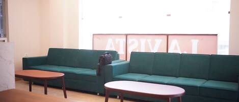 A room with a green sofa, two wooden tables, and a large window with a view.