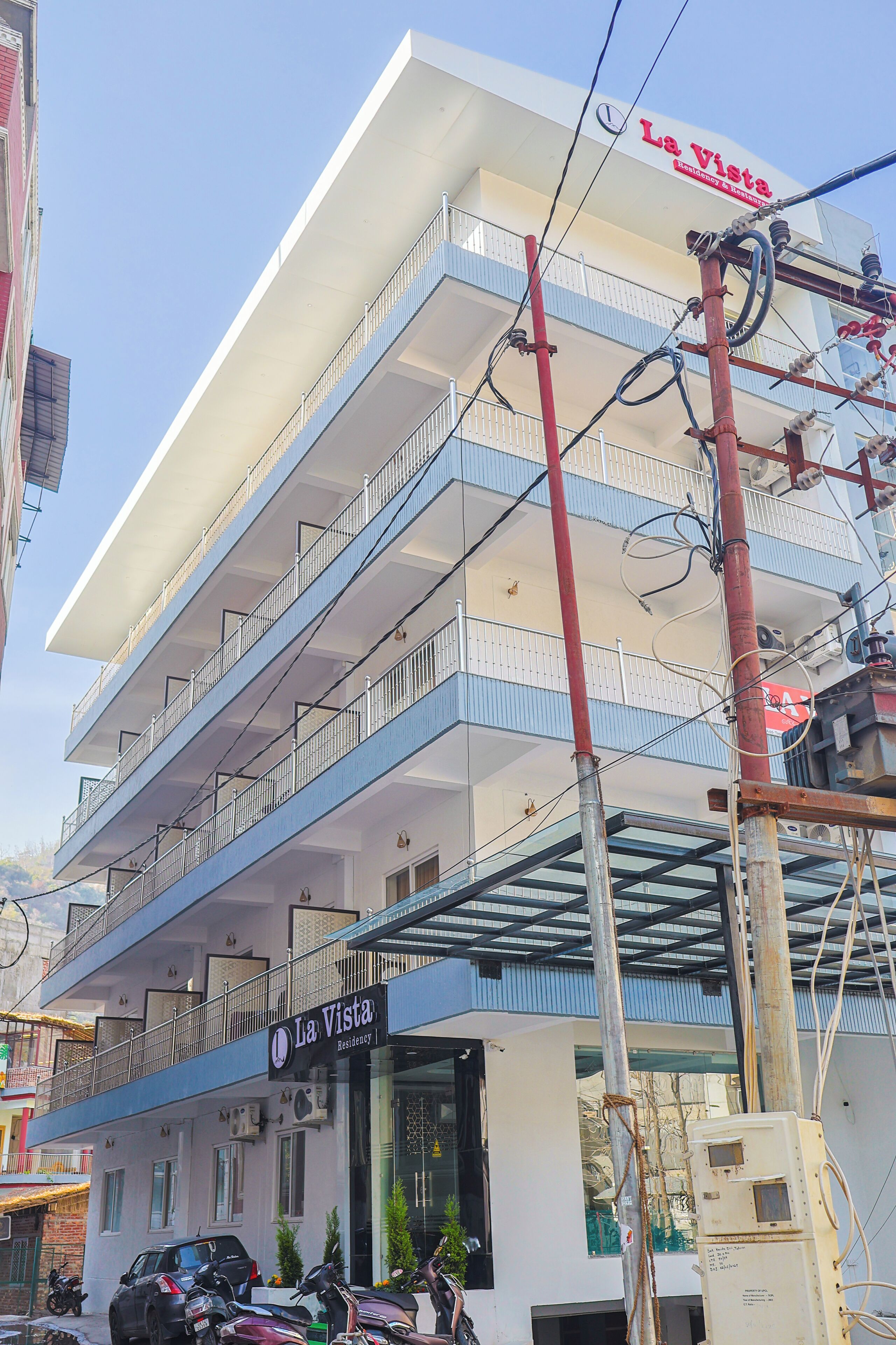 Un immeuble à plusieurs étages doté de balcons, une enseigne indiquant « La Vista Residencia », et des motos garées.