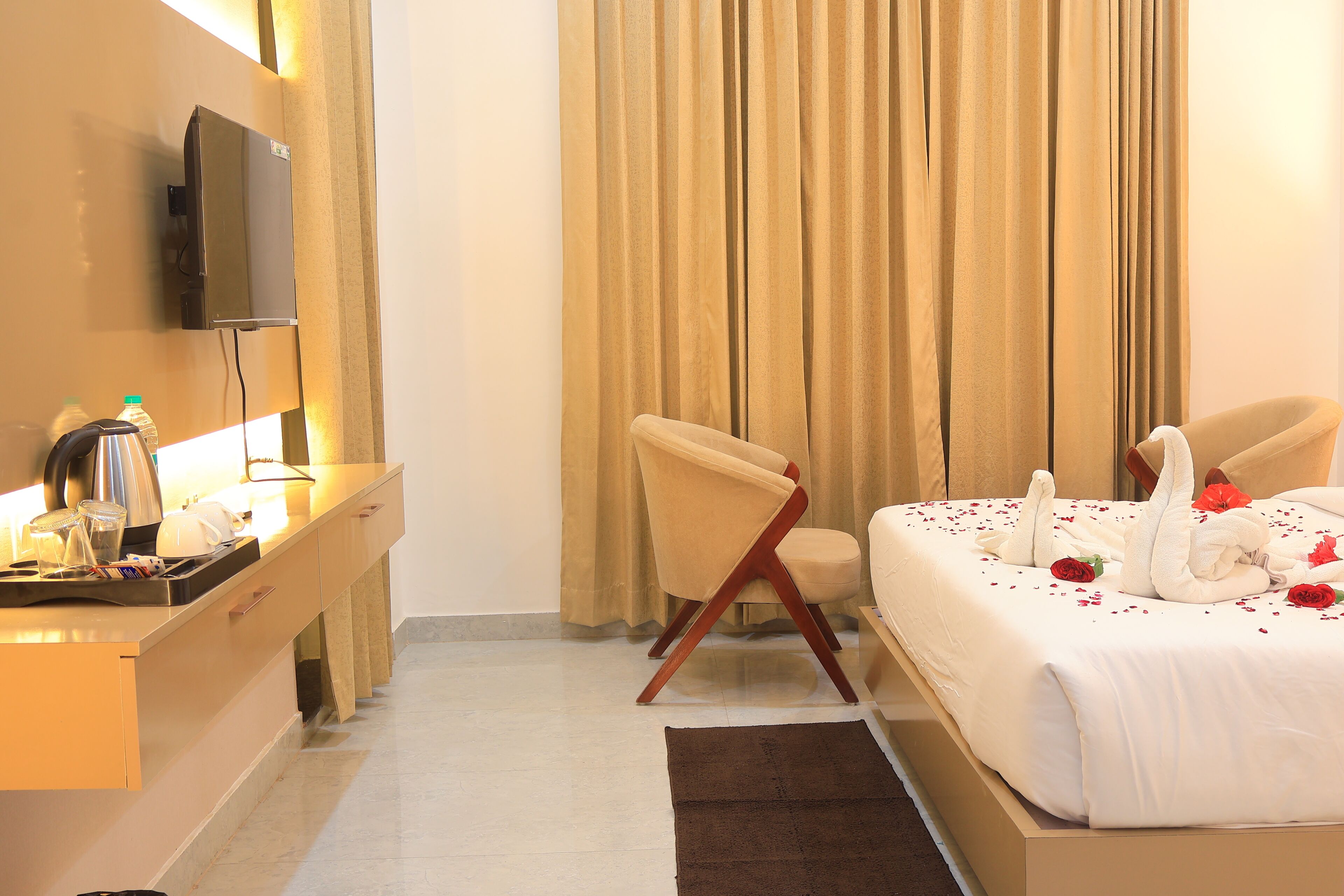 A hotel room with a bed, a desk with a flat-screen TV, a chair, and a window with curtains.