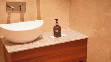Un baño con un lavamanos grande de color blanco, un mueble de tocador de madera y un dispensador de jabón en la encimera.