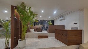 A modern lobby with a reception desk, seating area, and potted plants.