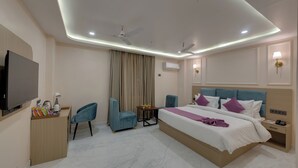 A modern hotel room with a large bed, two chairs, a desk with a flat-screen TV, and a ceiling fan.