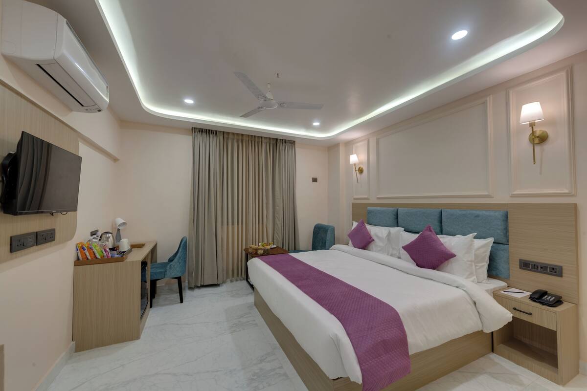 A modern hotel room with a bed, desk, chair, and a TV mounted on the wall.