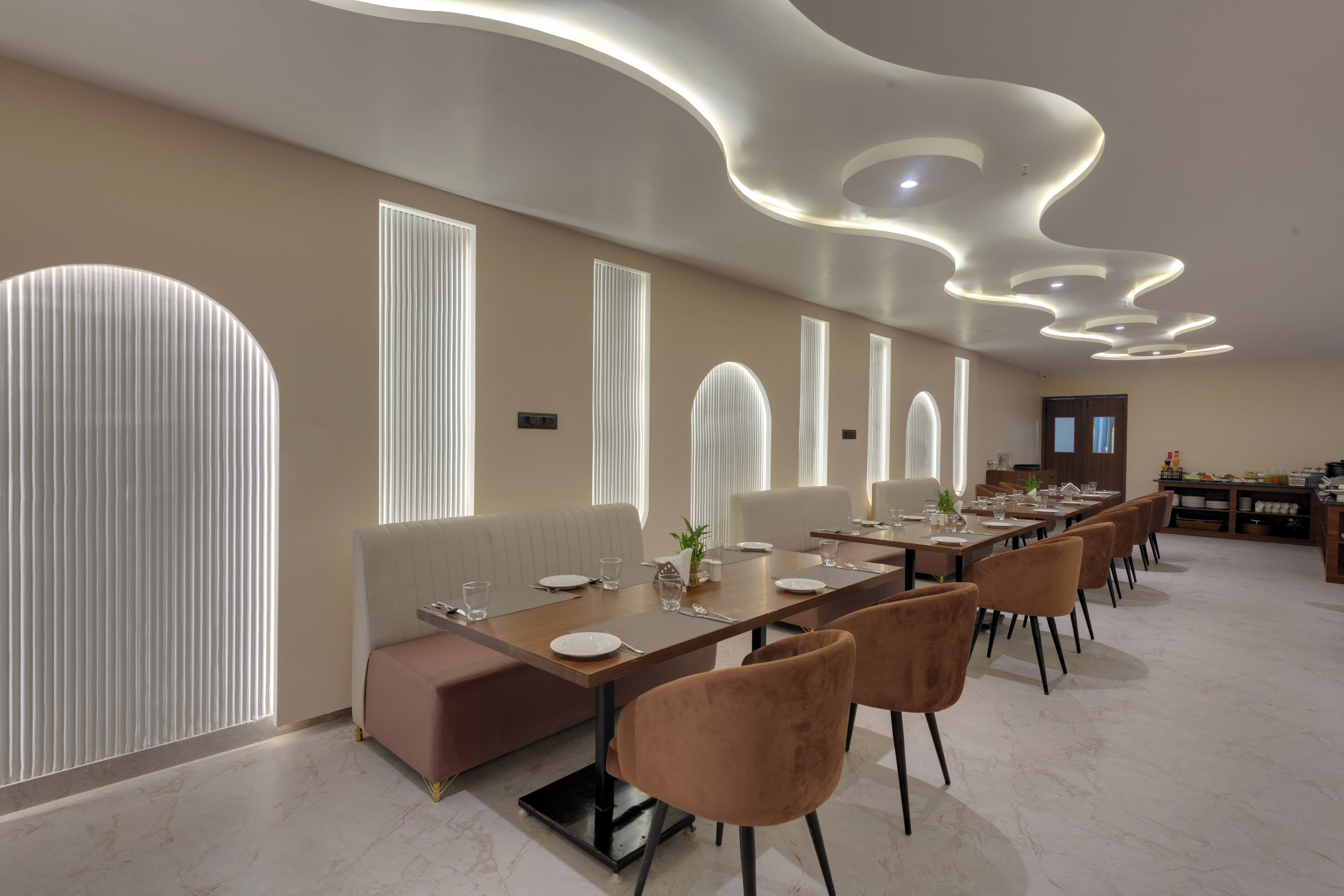 A modern dining area with a long table, cushioned seating, and contemporary ceiling design.