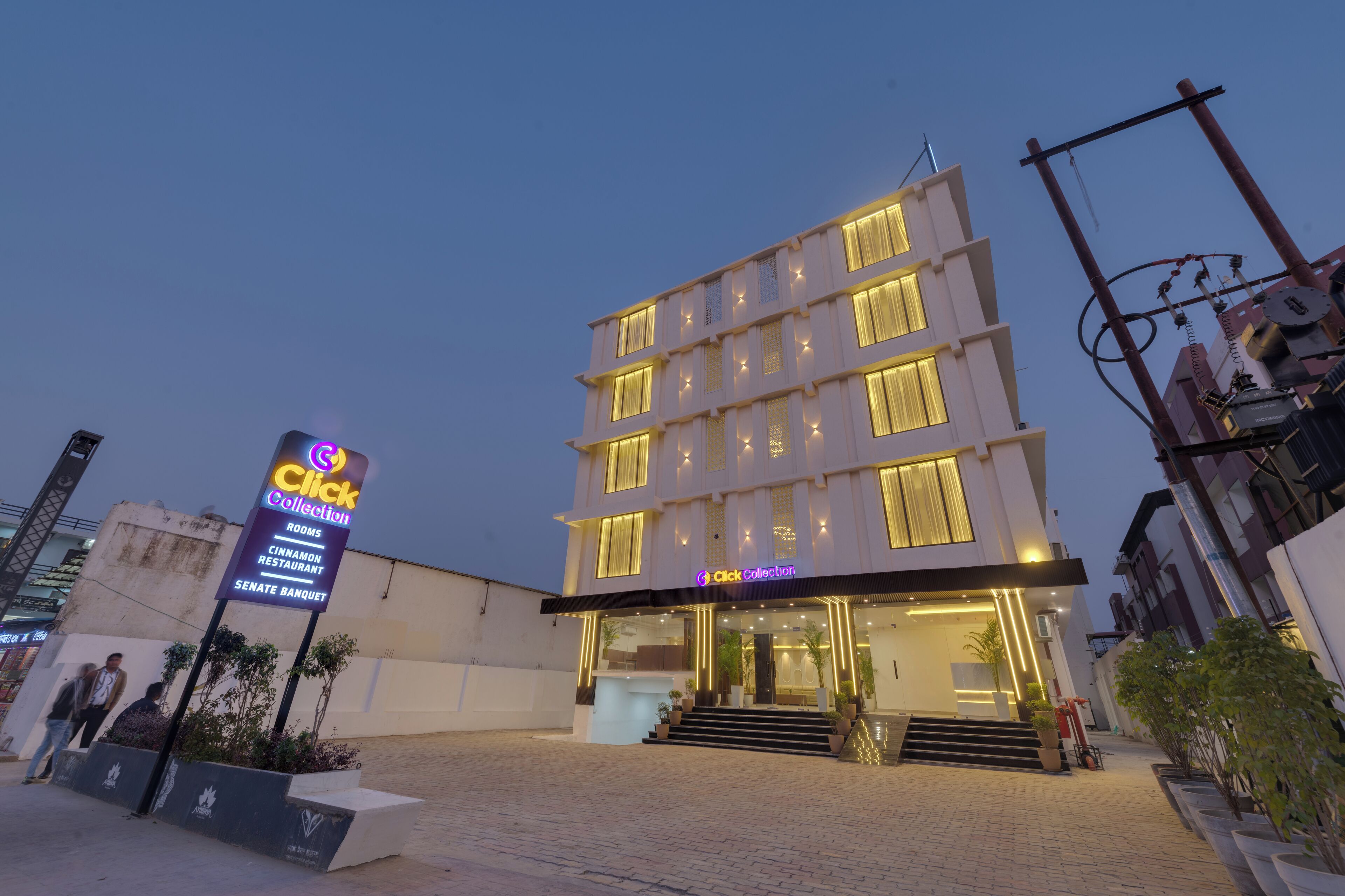 Un hotel de varios pisos con una entrada bien iluminada y un cartel que indica servicios como habitaciones, un restaurante y un salón de banquetes.