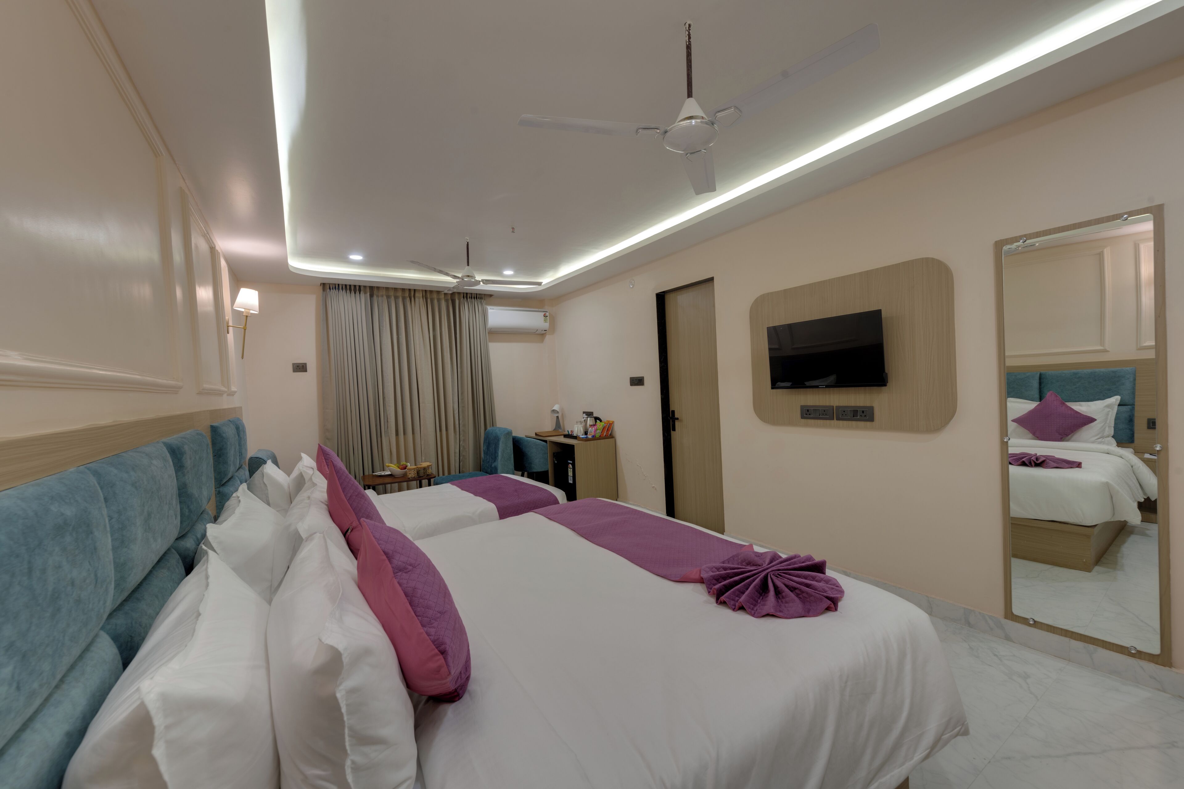 Ein Hotelzimmer mit zwei Betten, einem Fernseher, einem Deckenventilator und einem Spiegel.