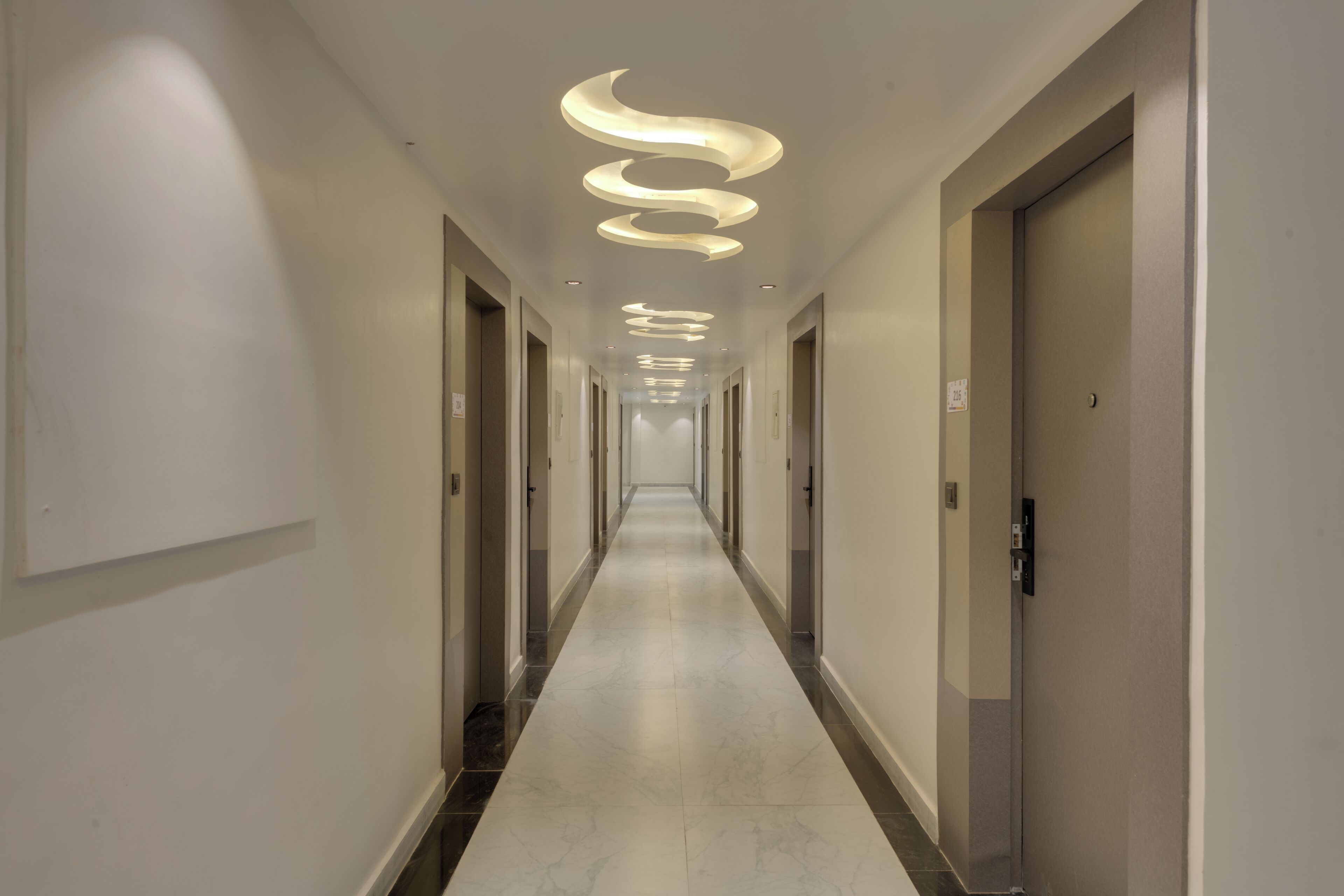 A long, narrow hallway with a modern spiral light fixture on the ceiling and doors on both sides.