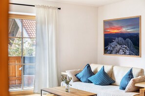 Una sala de estar con un sofá, una mesa de centro, una ventana con cortinas y un cuadro en la pared.