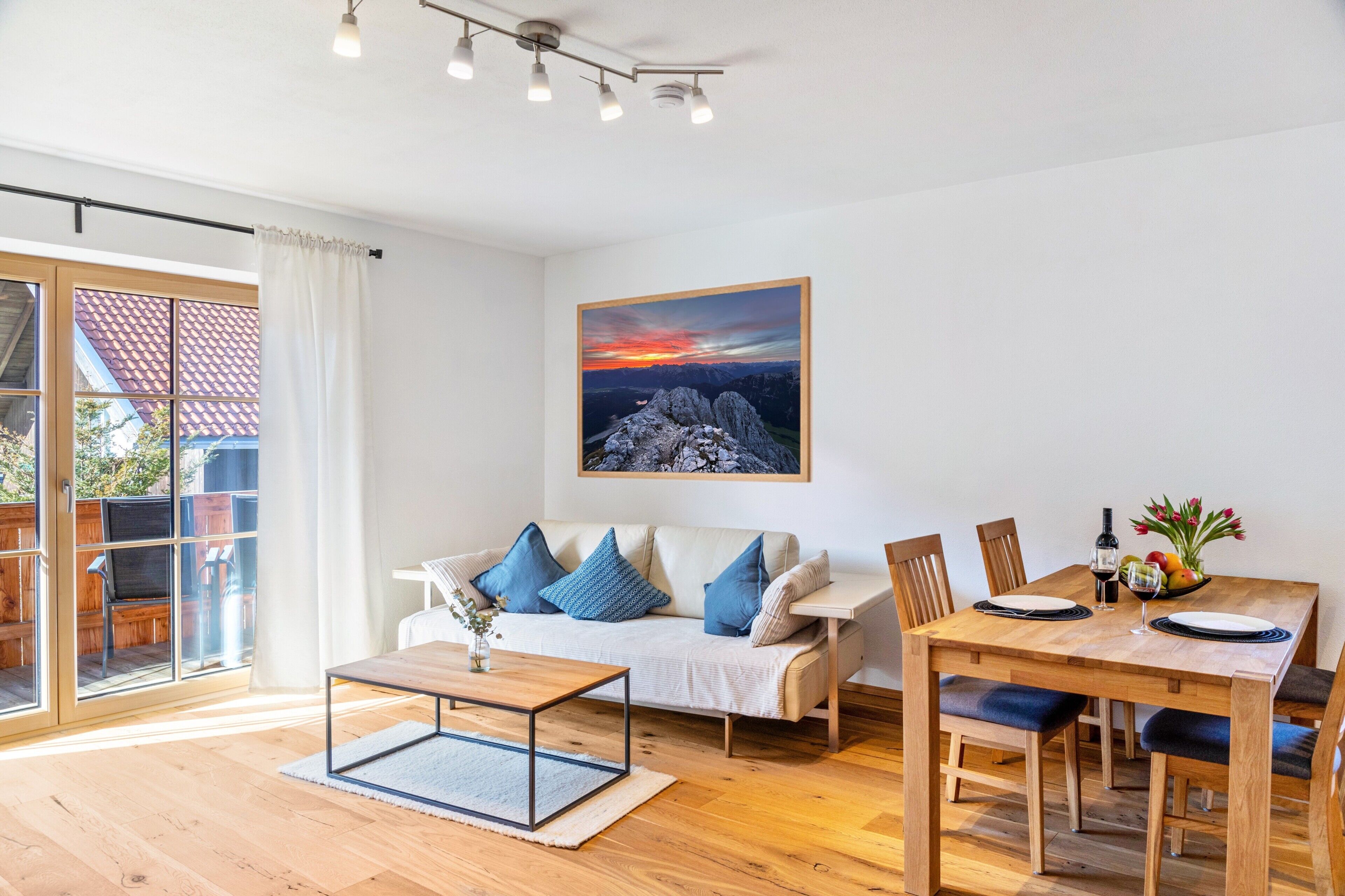 Ein modernes Wohnzimmer mit Sofa, Esstisch und Stühlen, einem Bild an der Wand und Blick durch eine Glastür.