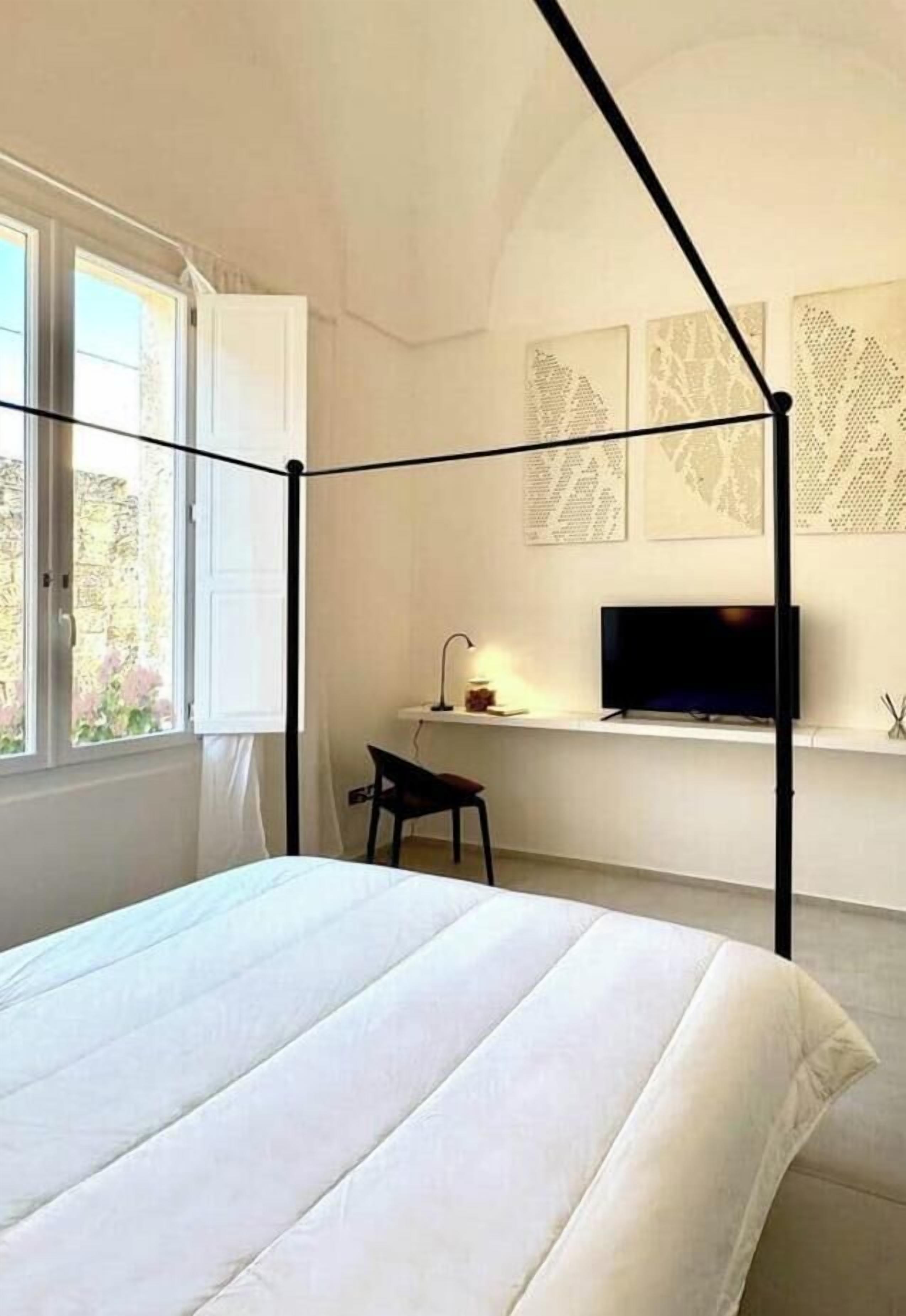 Een slaapkamer met een hemelbed, een bureau met stoel, een televisie en kunst aan de muur.