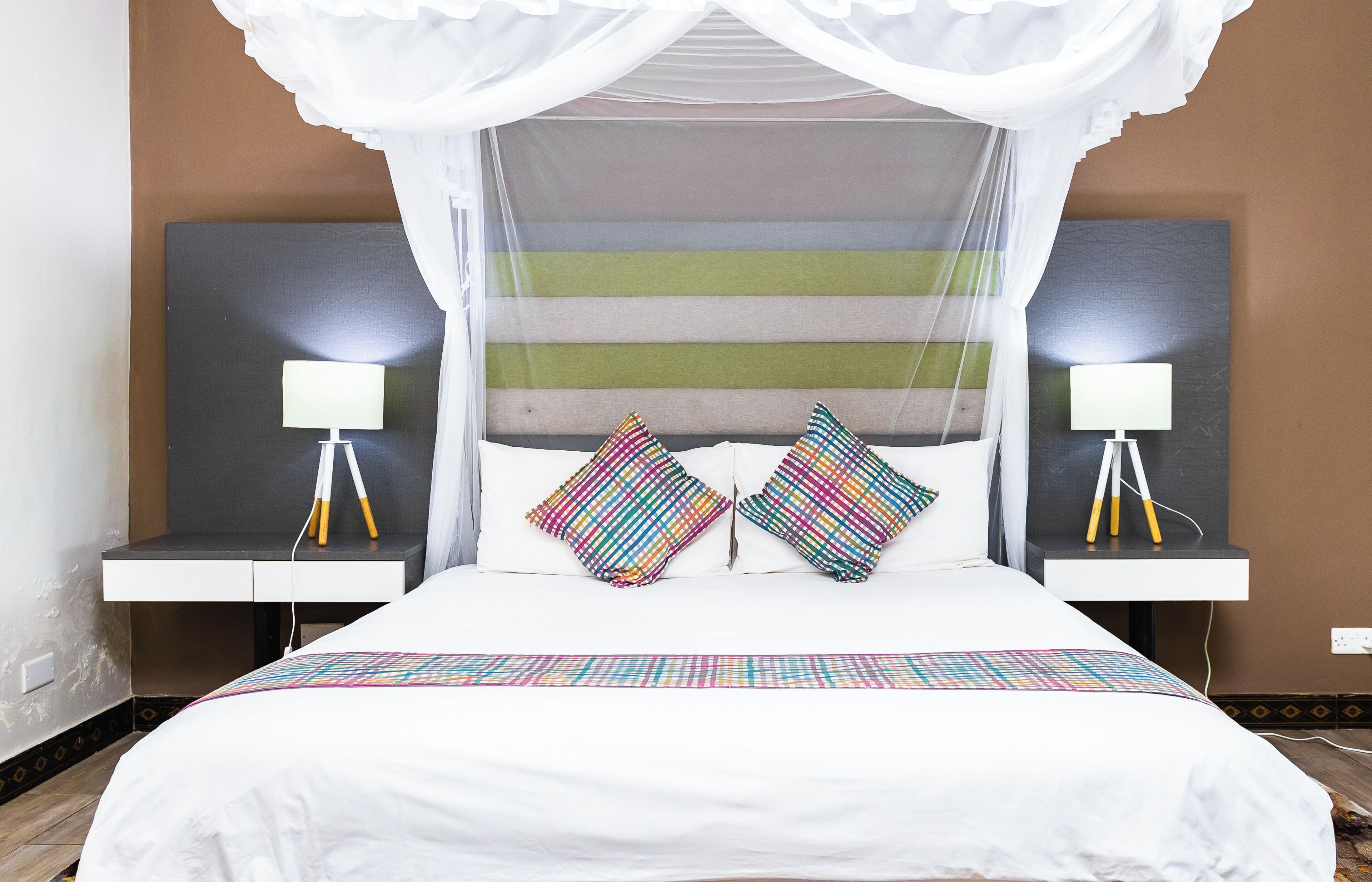 A bed with a canopy, two bedside lamps, and striped wall art.