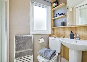 Ein Badezimmer mit Toilette, Waschbecken, Handtuchhalter und Ablage für Kosmetikartikel.