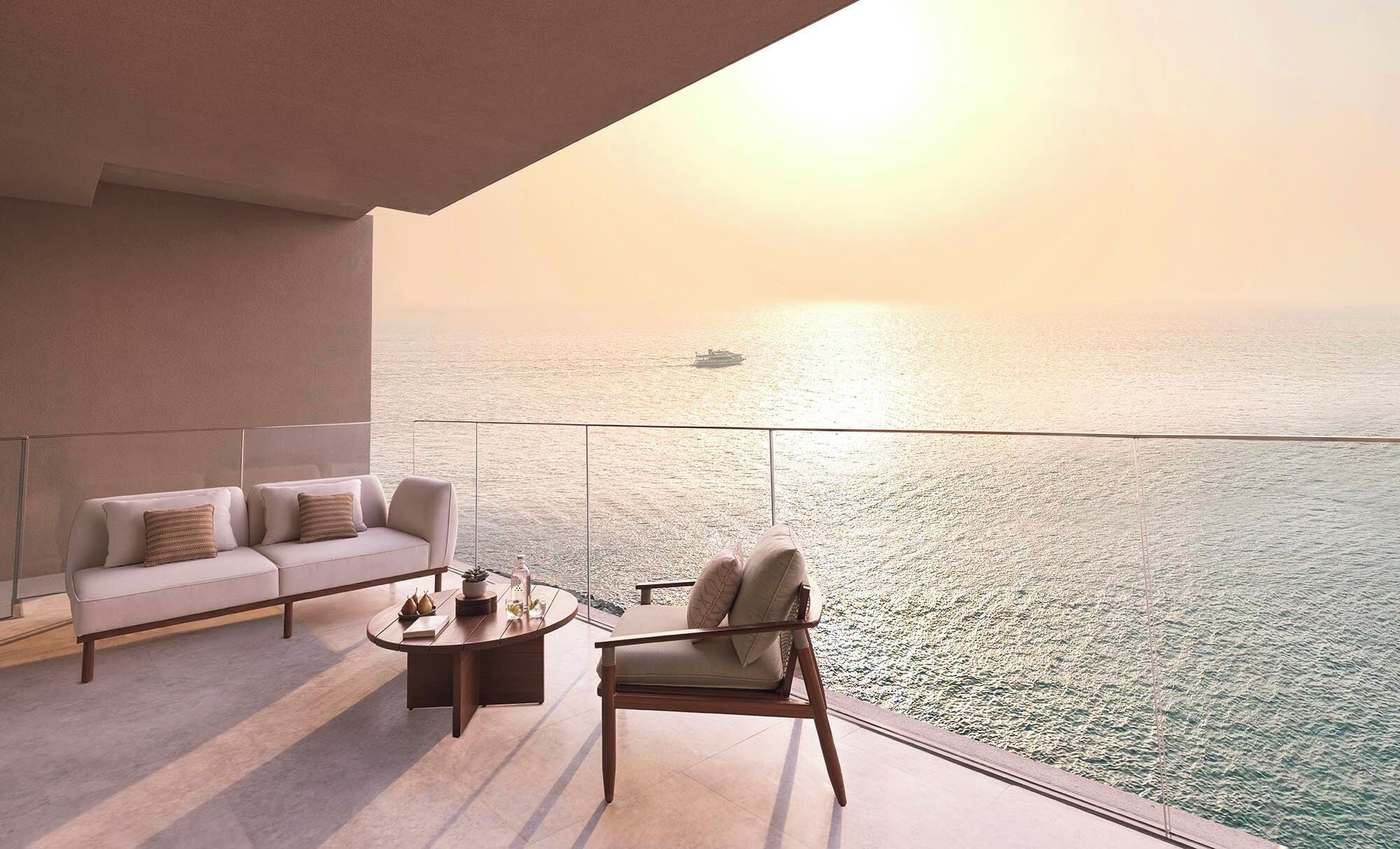 Un balcon avec un canapé et un fauteuil, une table basse, et une vue sur la mer avec un bateau à l’horizon.