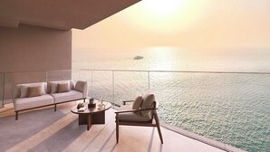 Ein Balkon mit einer Couch, einem Sessel, einem Couchtisch und Blick auf das Meer mit einem Schiff in der Ferne.