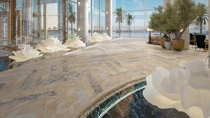 Eine großzügige Lobby mit einer imposanten Wasserspüle, einer hohen Decke mit einer außergewöhnlichen Leuchte und großen Fenstern mit Blick auf Palmen.