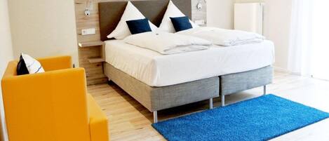 Een moderne hotelkamer met een bed, een blauw vloerkleed en een gele fauteuil.