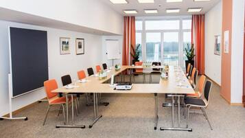 A conference room with a long table, chairs, a whiteboard, and large windows with curtains.