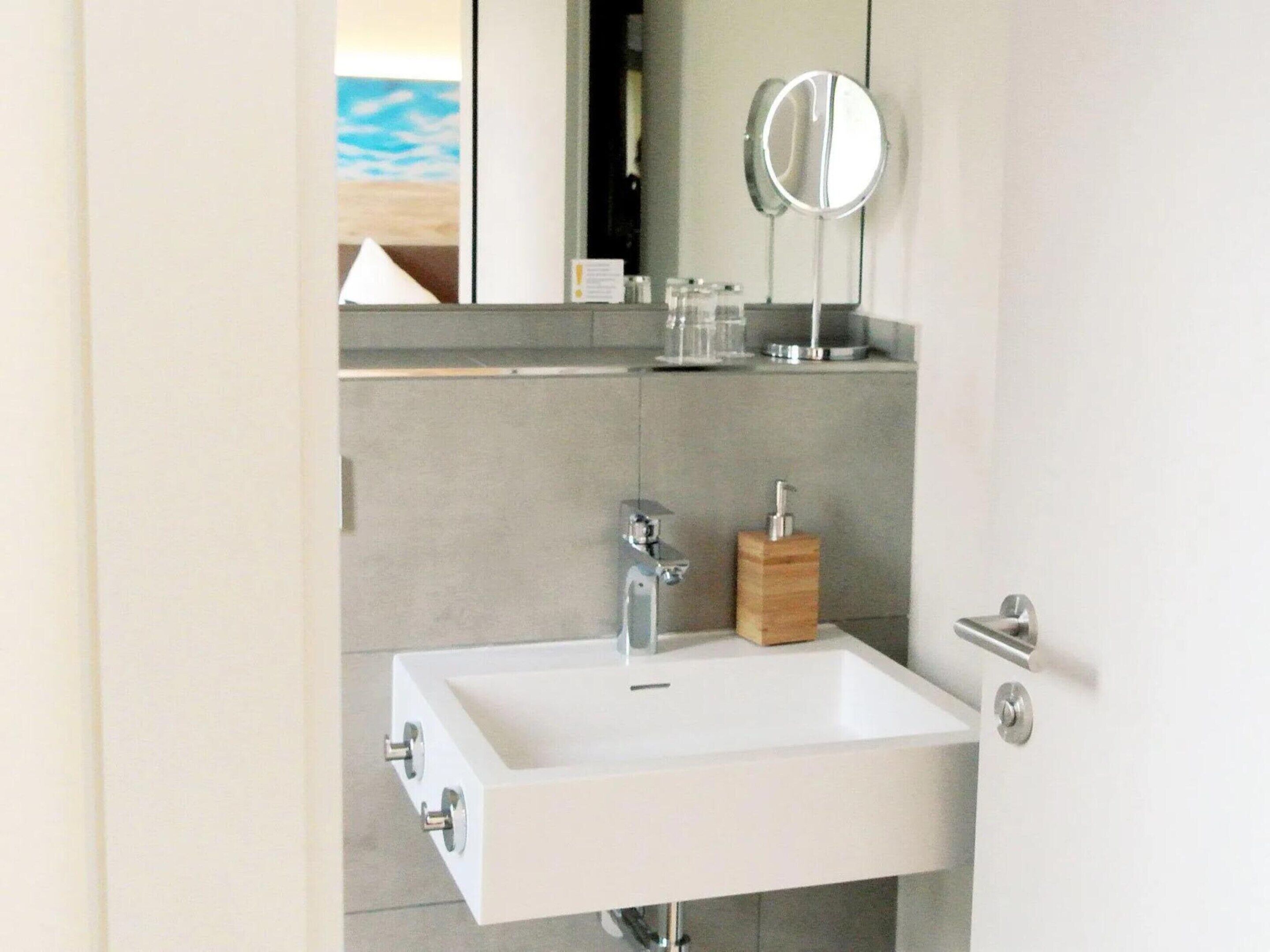 Une salle de bain moderne avec un lavabo blanc, un miroir et un distributeur de savon en bois.