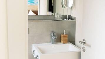 Une salle de bain moderne avec un lavabo blanc, un miroir et un distributeur de savon en bois.