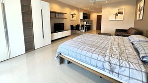 A modern bedroom with a large bed, a TV, a desk, and a kitchenette. - Sea View Studio With Large Balcony at View Talay 5D (Pattaya)