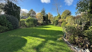 Un jardin bien entretenu, agrémenté de divers arbustes et arbres, sous un ciel bleu dégagé, et avec une pelouse parfaitement taillée.