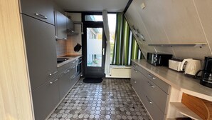 Une cuisine compacte avec des meubles gris, un sol carrelé et une vue sur l’extérieur par la porte.