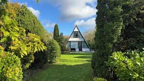 Une maison moderne avec un toit triangulaire, entourée d’une végétation luxuriante et d’une pelouse bien entretenue.