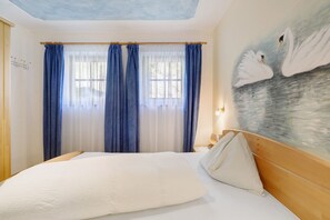 Ein Schlafzimmer mit Bett, Vorhängen, einem Wandbild und einem Fenster.