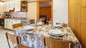 Comedor con mesa dispuesta para cuatro, cocina al fondo y puerta de madera que da a otra habitación.