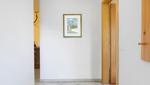 Un pasillo con un cuadro enmarcado en la pared, una puerta de madera y un suelo de baldosas.
