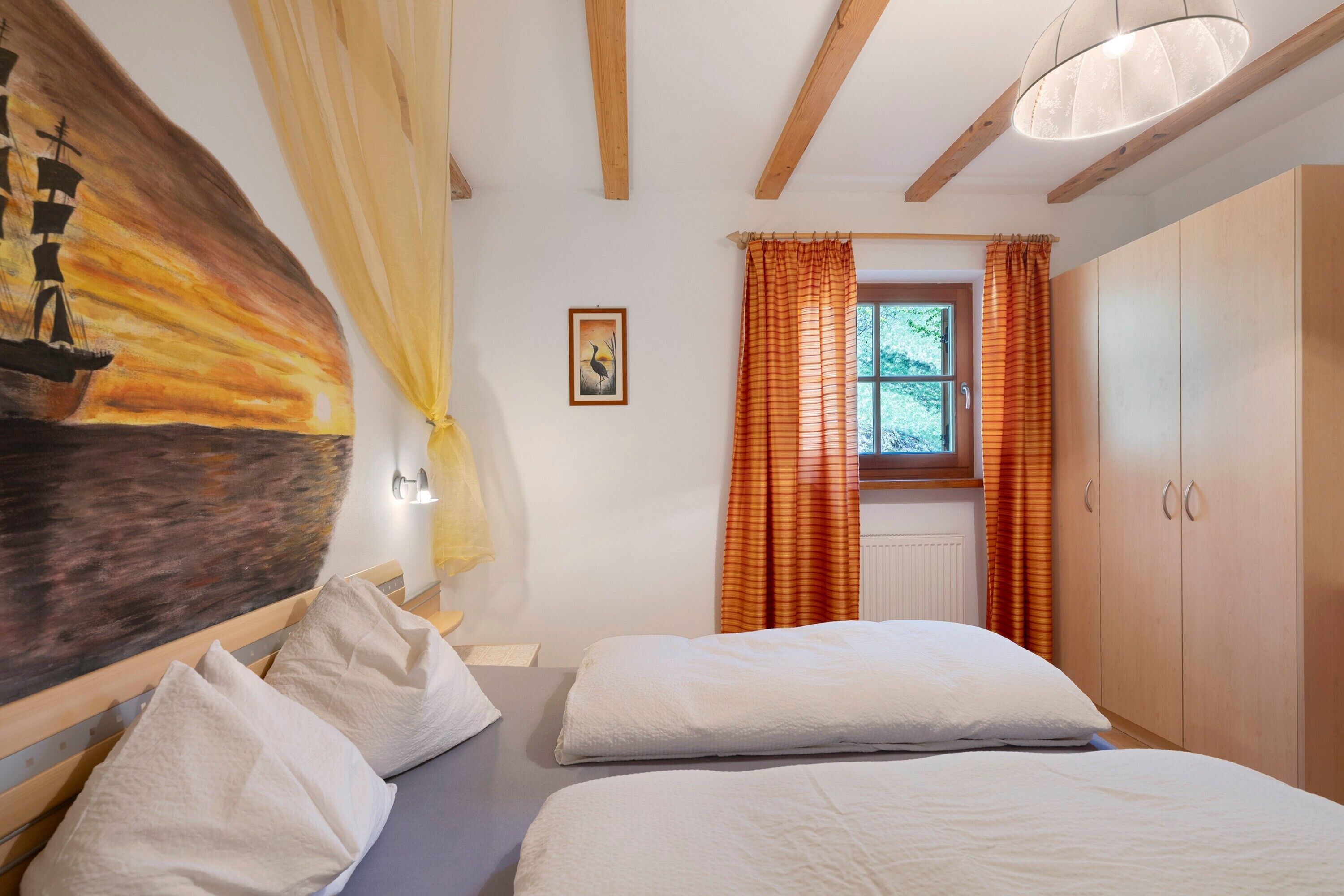A bedroom with two beds, a painting, a window with curtains, and wooden beams on the ceiling.