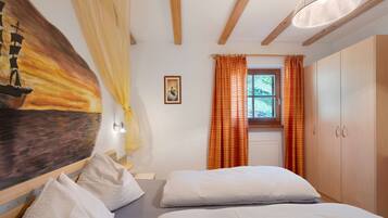 A bedroom with two beds, a painting, a window with curtains, and wooden beams on the ceiling.