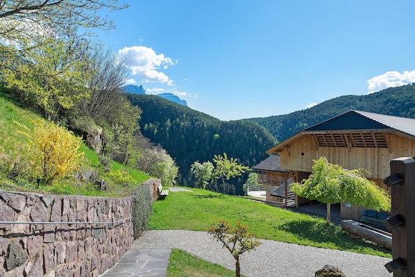 A stone wall, a wooden building, and a paved path in a mountainous area. - Grafaierhof Apartment 'Engel' with Mountain View (Kastelruth)