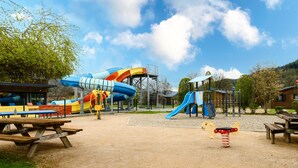 Une aire de jeux avec des toboggans et des balançoires, des tables de pique-nique et un espace de repos abrité.