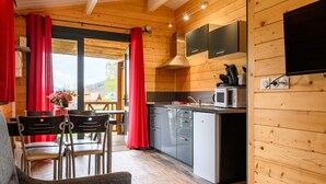 Une cuisine moderne aux murs en bois, un coin repas avec des chaises et une grande fenêtre agrémentée de rideaux.