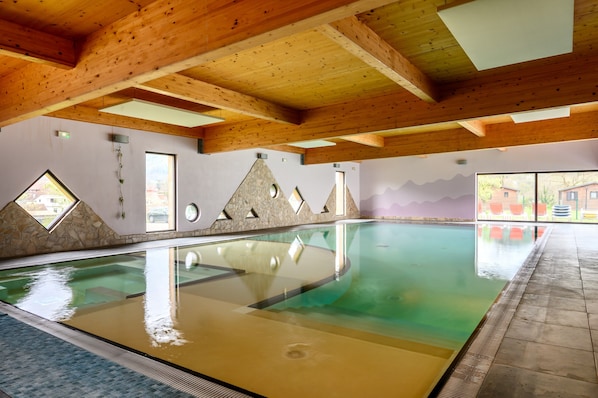 Une piscine intérieure avec des poutres en bois, des murs en pierre et de grandes fenêtres.
