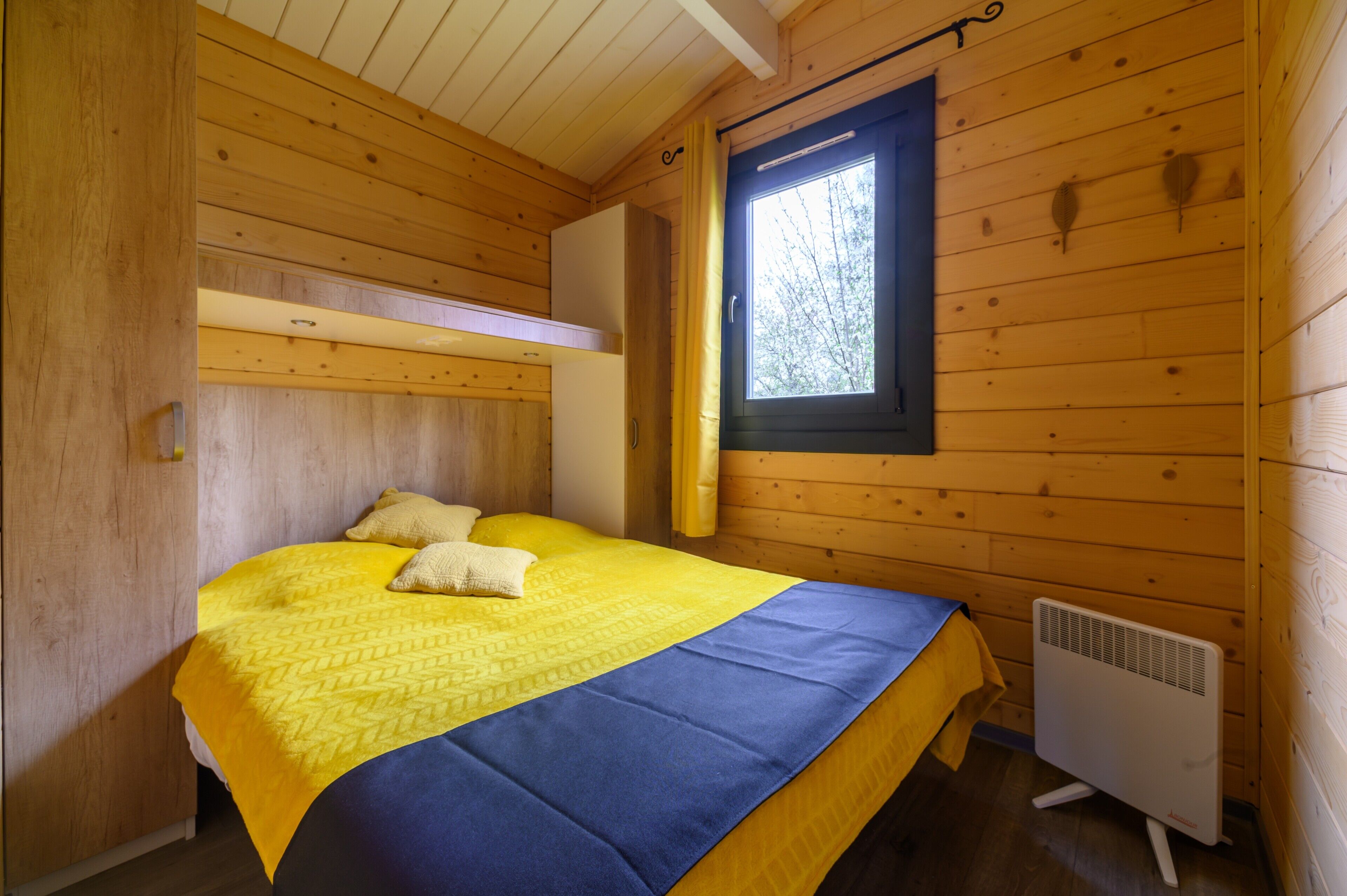 A wooden cabin room with a bed, a window, and a heater.