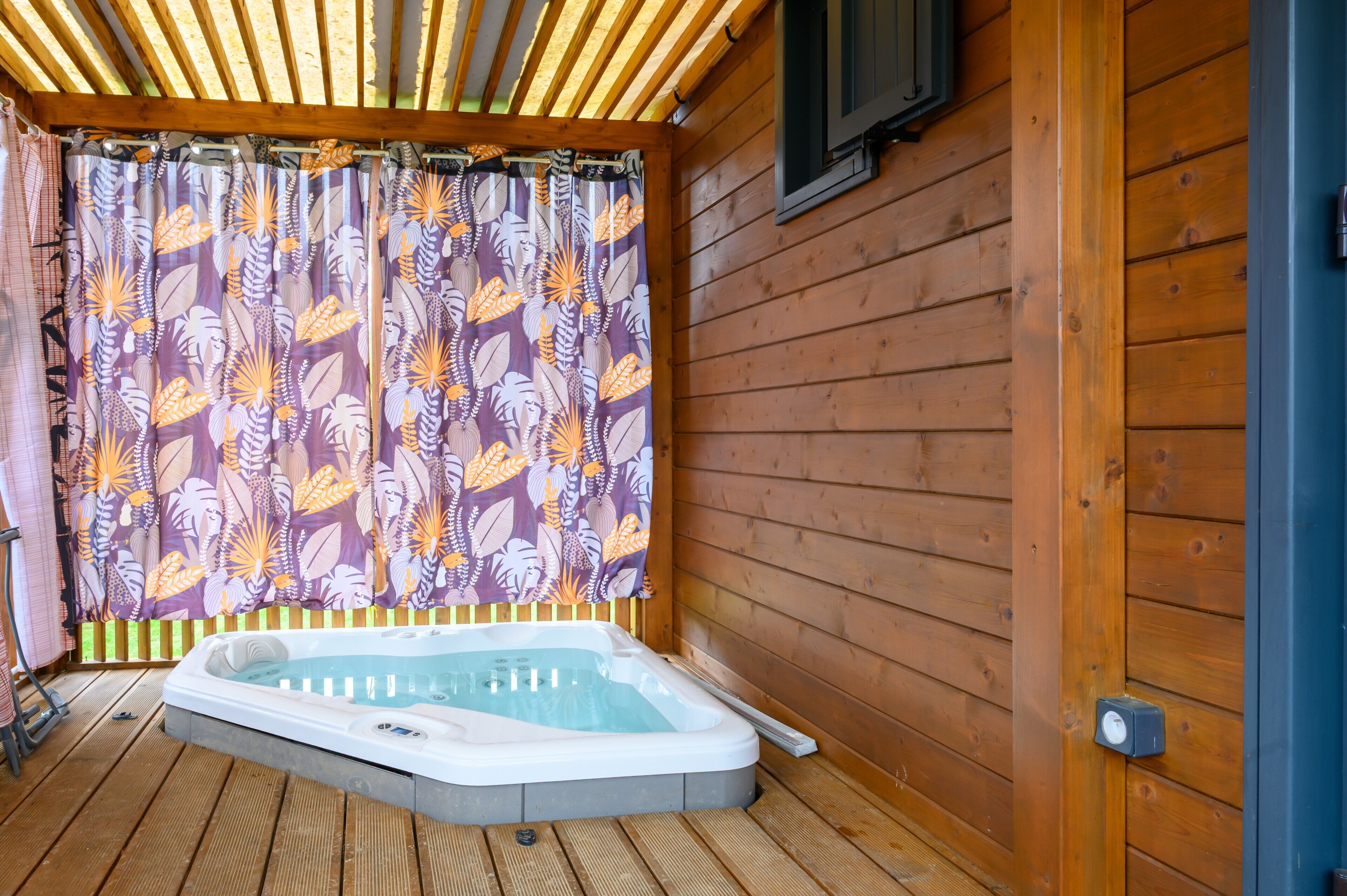 A wooden deck with a hot tub, wooden walls, and a curtain with a leaf pattern.