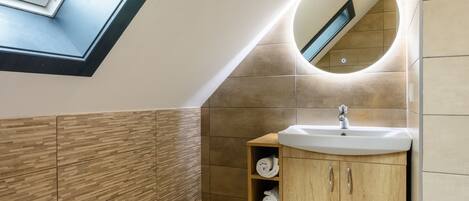 A modern bathroom with a skylight, a round mirror, a sink, and wooden cabinets.