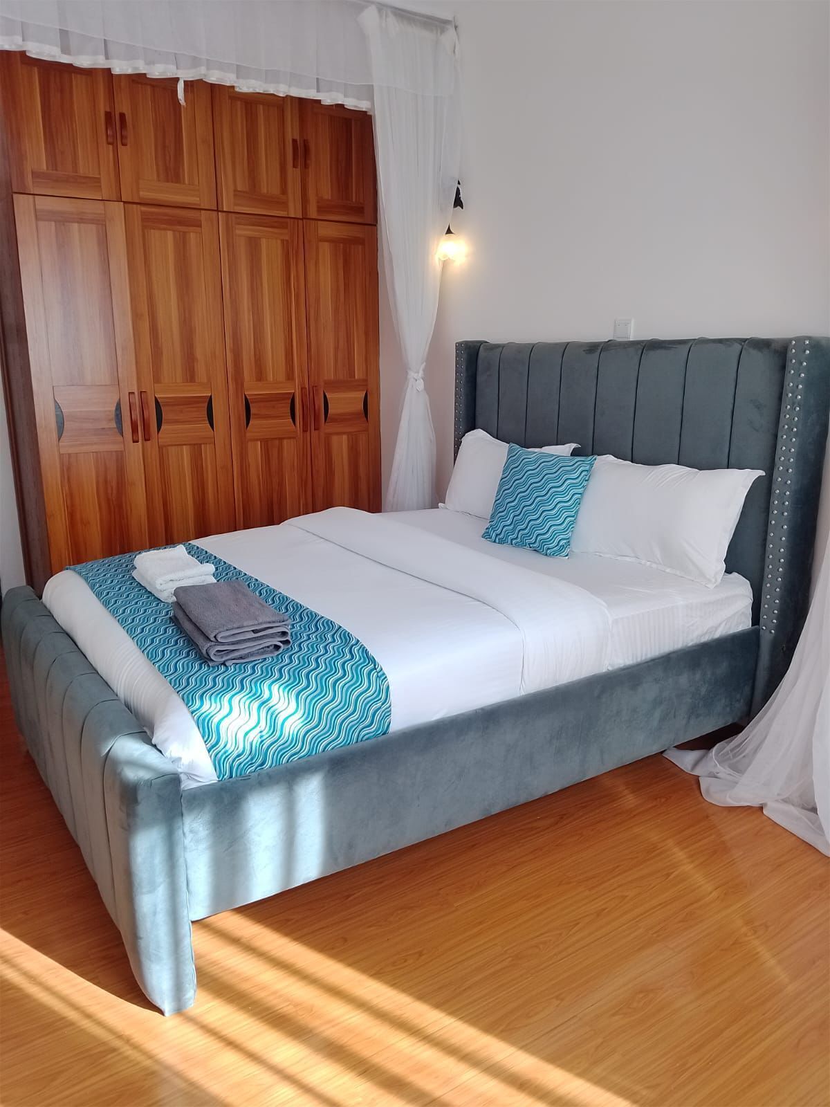 A neatly made bed with a grey headboard, white bedding, and a blue patterned throw.