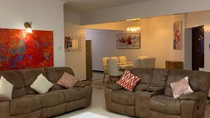 A modern living room with two brown sofas, a white coffee table, and a dining area in the background. - Peaceful 4bed all-ensuite apartment in vibrant Nairobi (Nairobi)