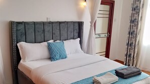 A neatly made bed with white and blue bedding, a grey upholstered headboard, and a bedside table with a lamp. - Peaceful 4bed all-ensuite apartment in vibrant Nairobi (Nairobi)