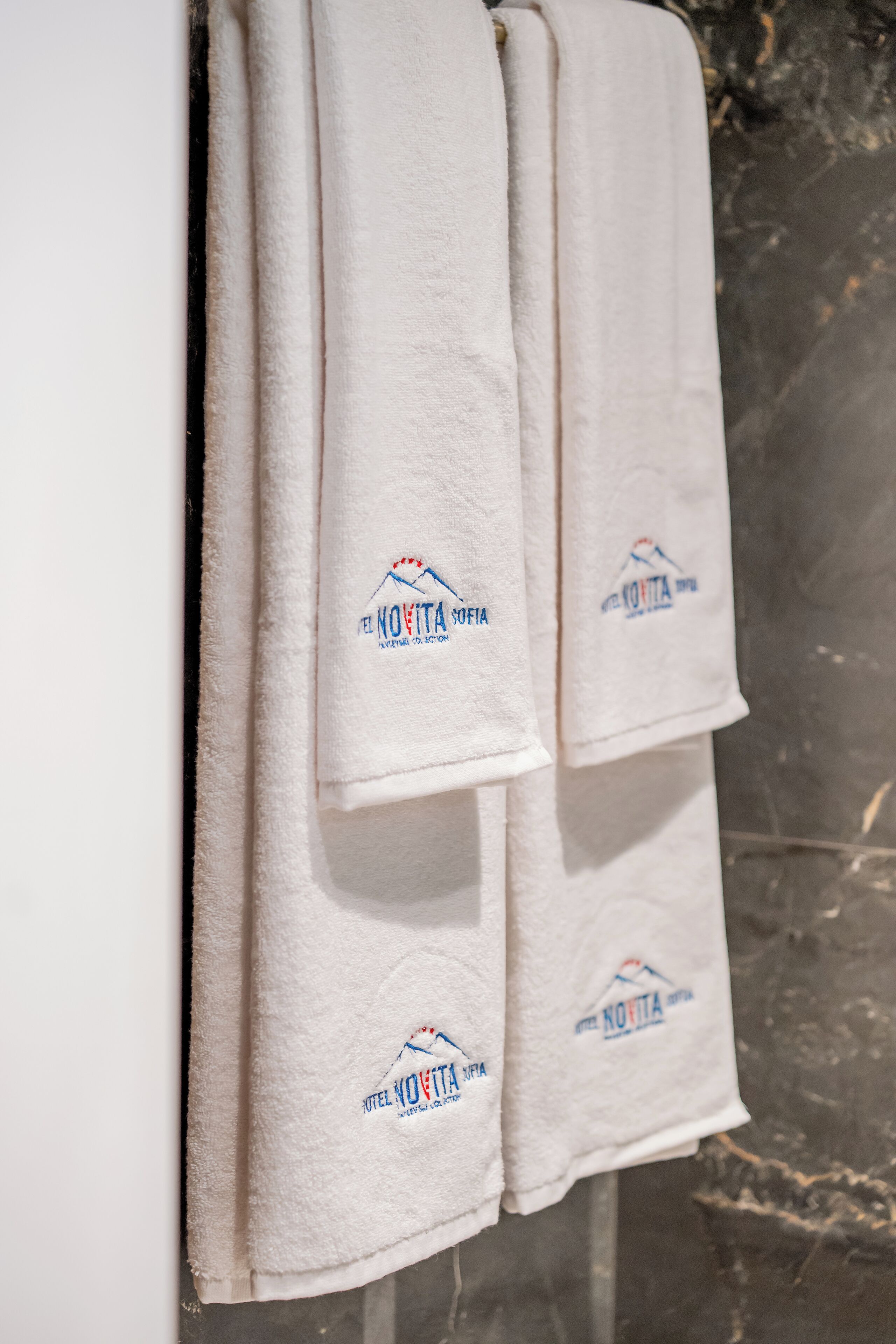 Tres toallas blancas colgadas en una pared, cada una con el logotipo que dice "HOTEL NOVITA".