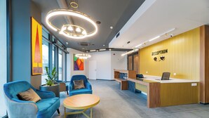 A reception area with a wooden reception desk, two blue armchairs, a small wooden table, and a large window providing natural light.